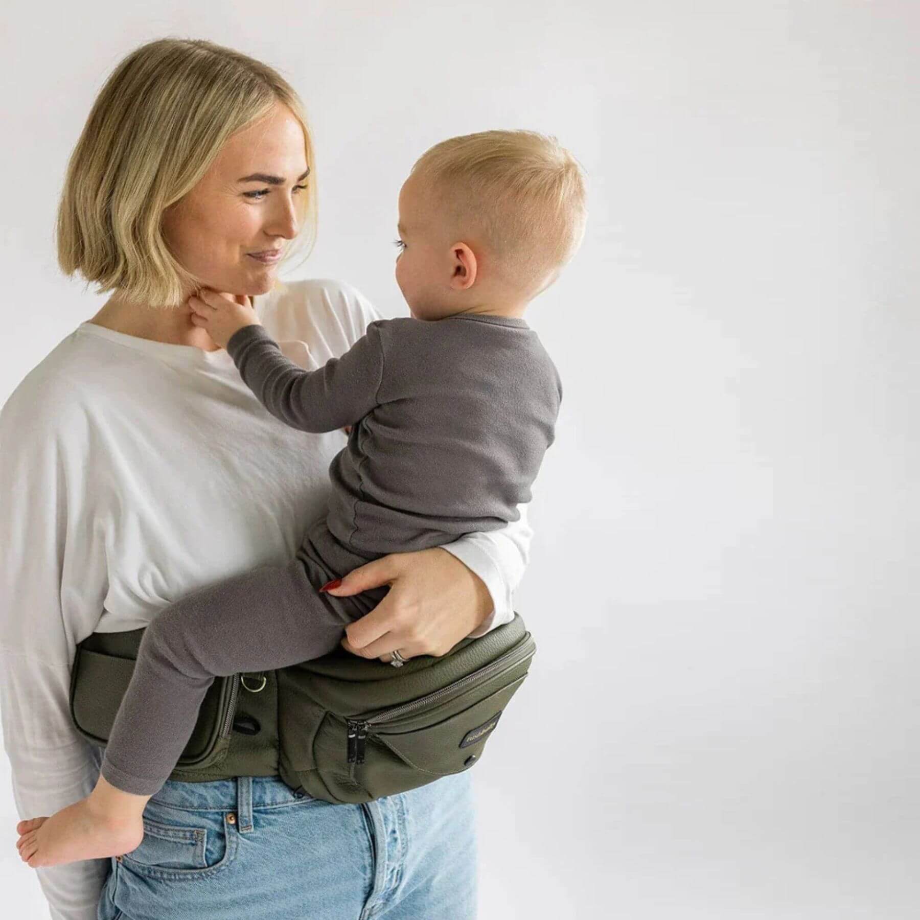 Woman holding a child using The Tushbaby Hip Carrier - Olive