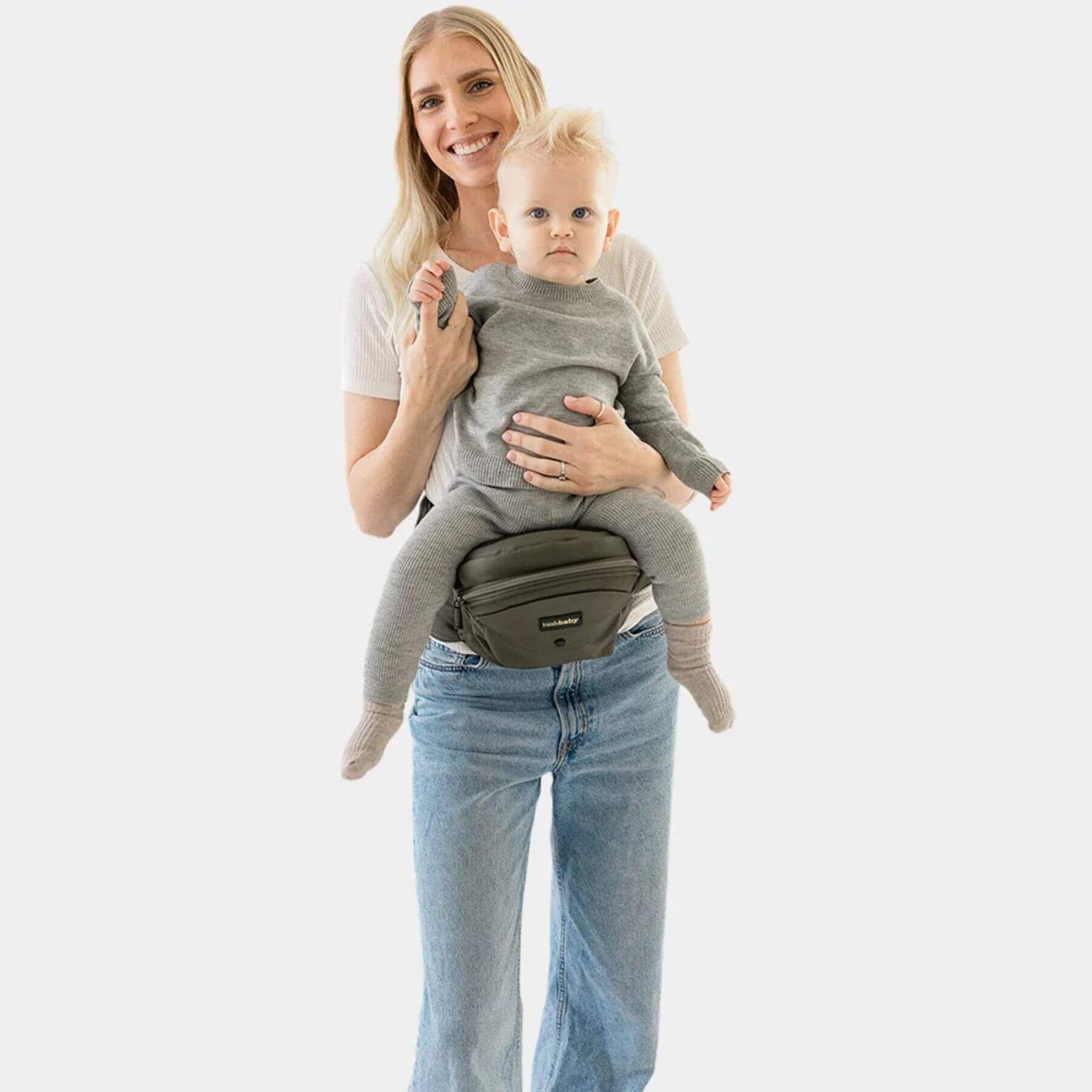 Woman holding a baby using The Tushbaby Hip Carrier - Olive