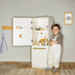 Child standing next to Tiny Land® Cabinet Play Fridge in a room with a framed picture on the wall.