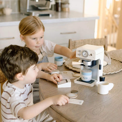 Two children playing with Tiny Land® Children’s Coffee Maker on a wooden table.