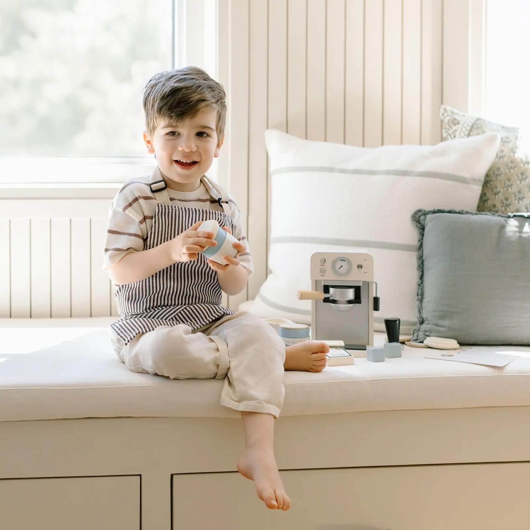 Child sitting on a window sill holding a toy, with Tiny Land® Children’s Coffee Maker