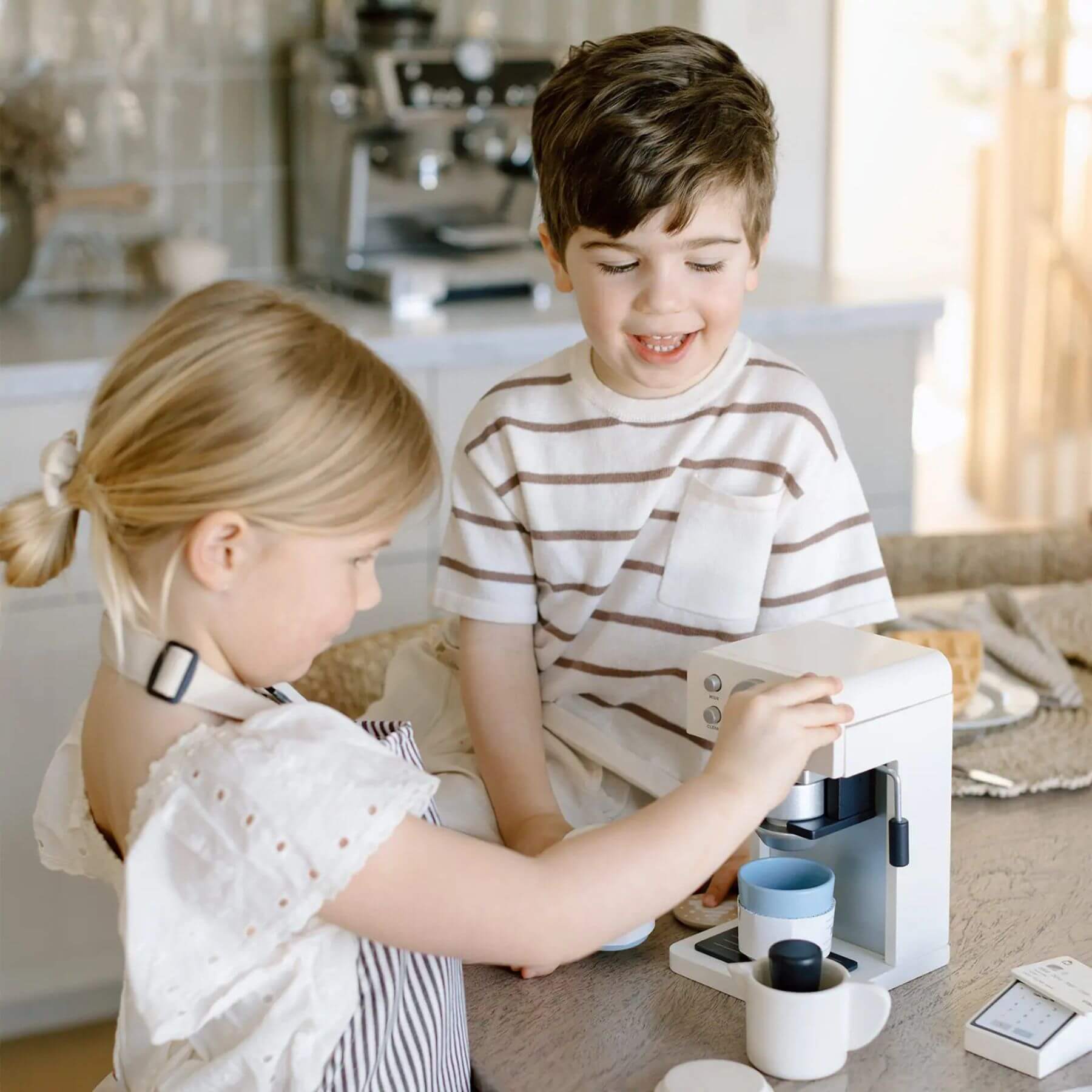 Two children playing with Tiny Land® Children’s Coffee Maker in a kitchen setting.