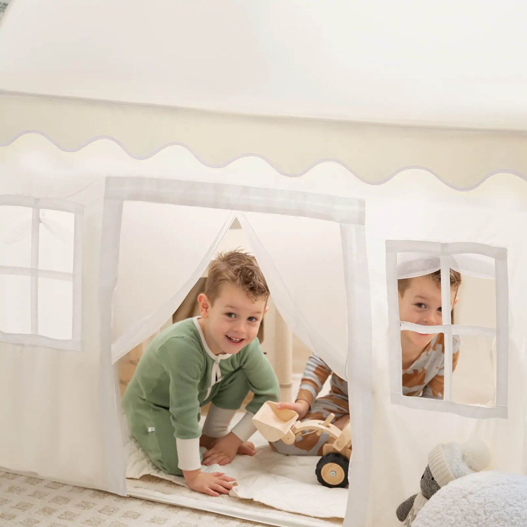 Two children playing inside aTiny Land® Playhouse Tent – Natural Cream in a room with a bed and window.