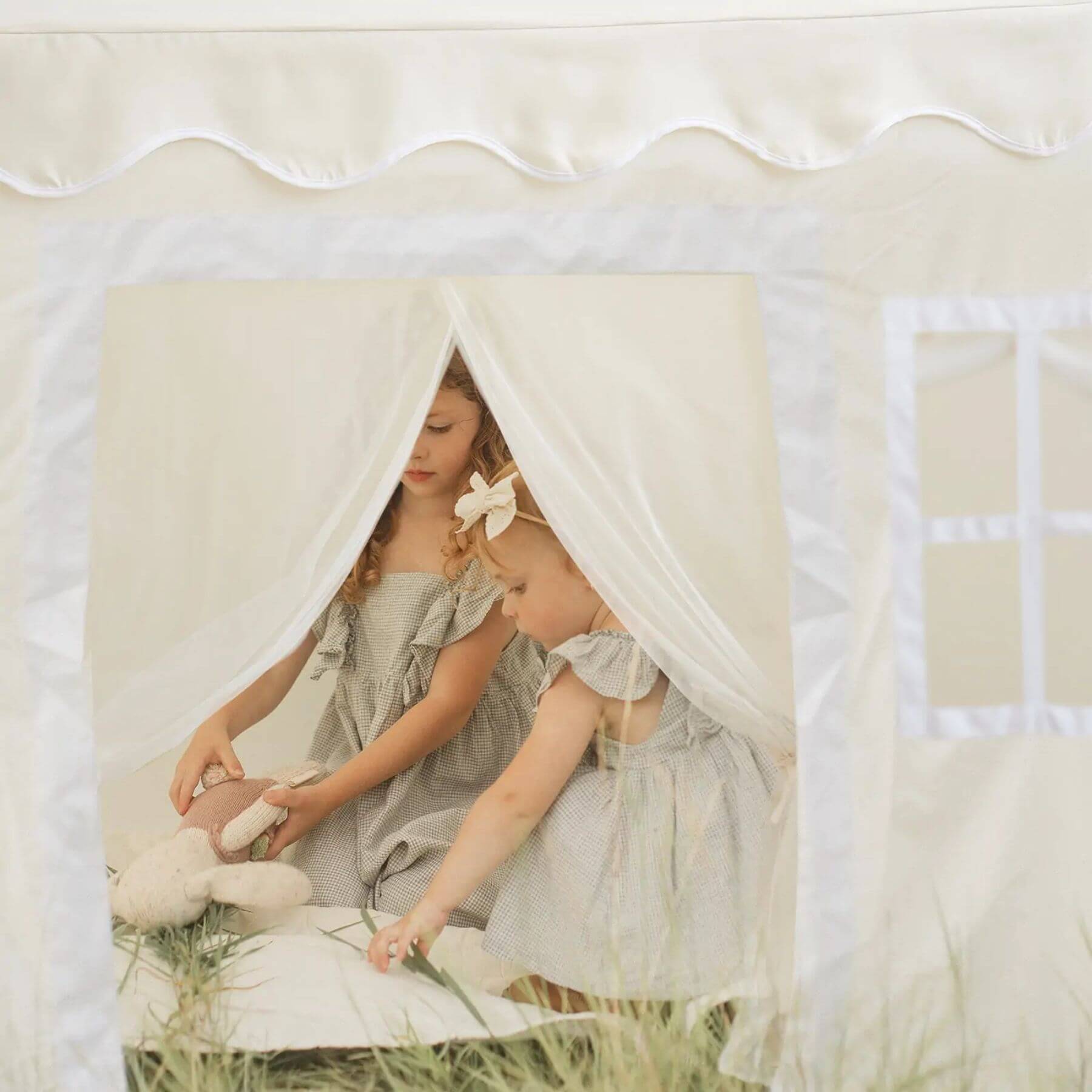 Two young girls in matching dresses playing inside Tiny Land® Playhouse Tent – Natural Cream