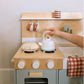 Wooden toy kitchen set with a child's hand placing a white teapot on a stove.