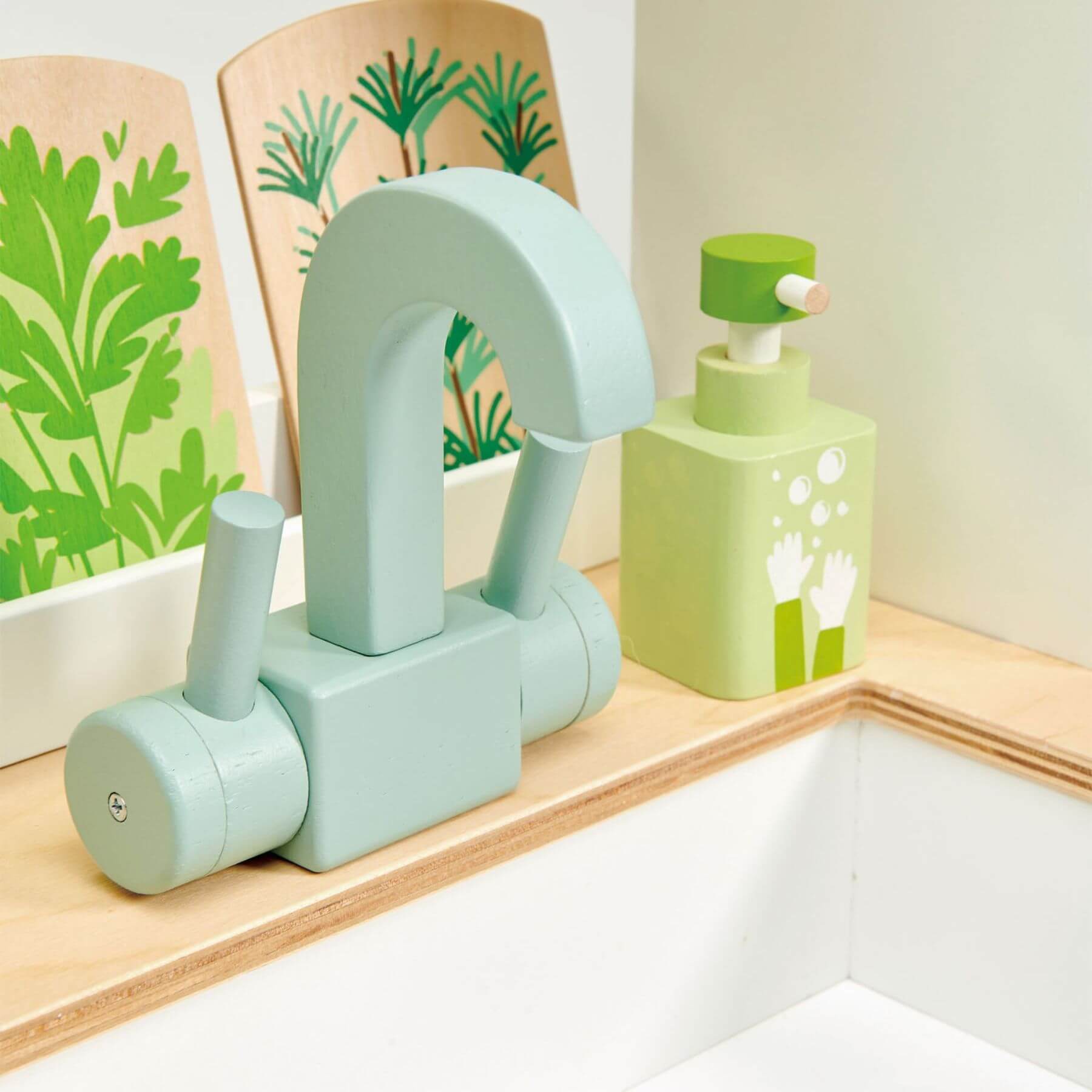 Toy Green kitchen sink strainer and soap dispenser on a wooden shelf with a floral-patterned backsplash.