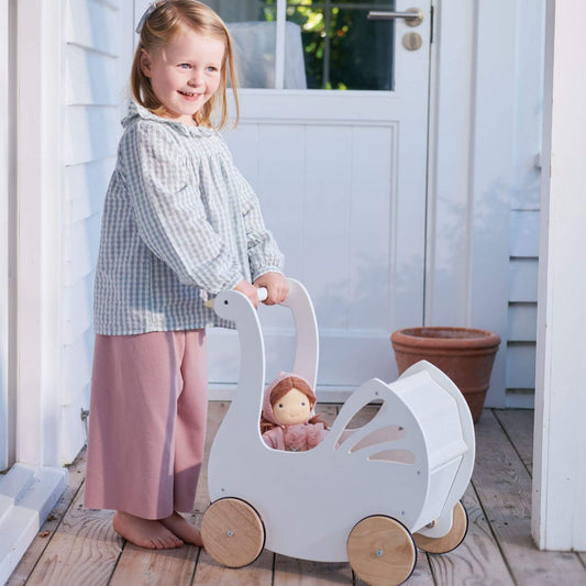 Child holding Tender Leaf Sweet Swan Pram with a doll inside on a wooden deck.