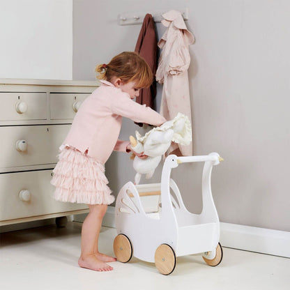 Child playing with Tender Leaf Sweet Swan Pram in a room with white dresser and pink clothing.