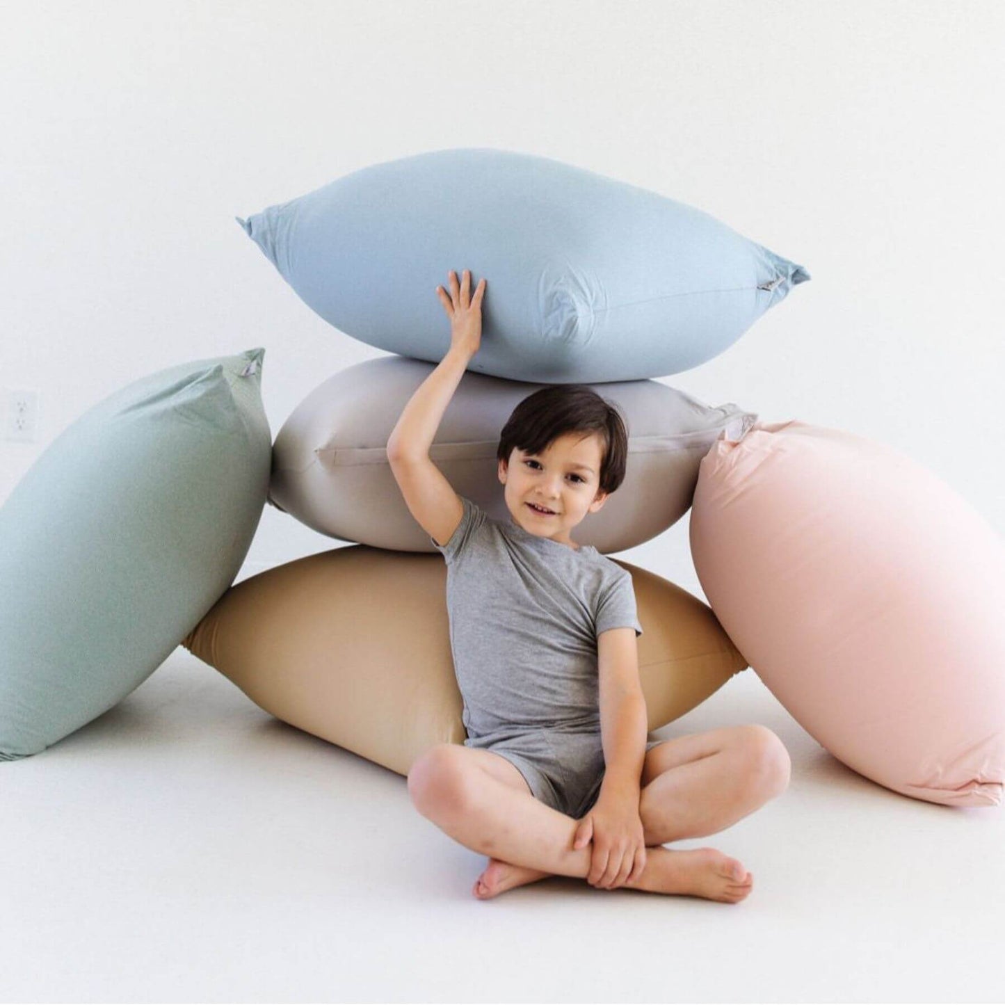 A young child sits cross-legged in the center of a stack of Toki Kids Bean Bags