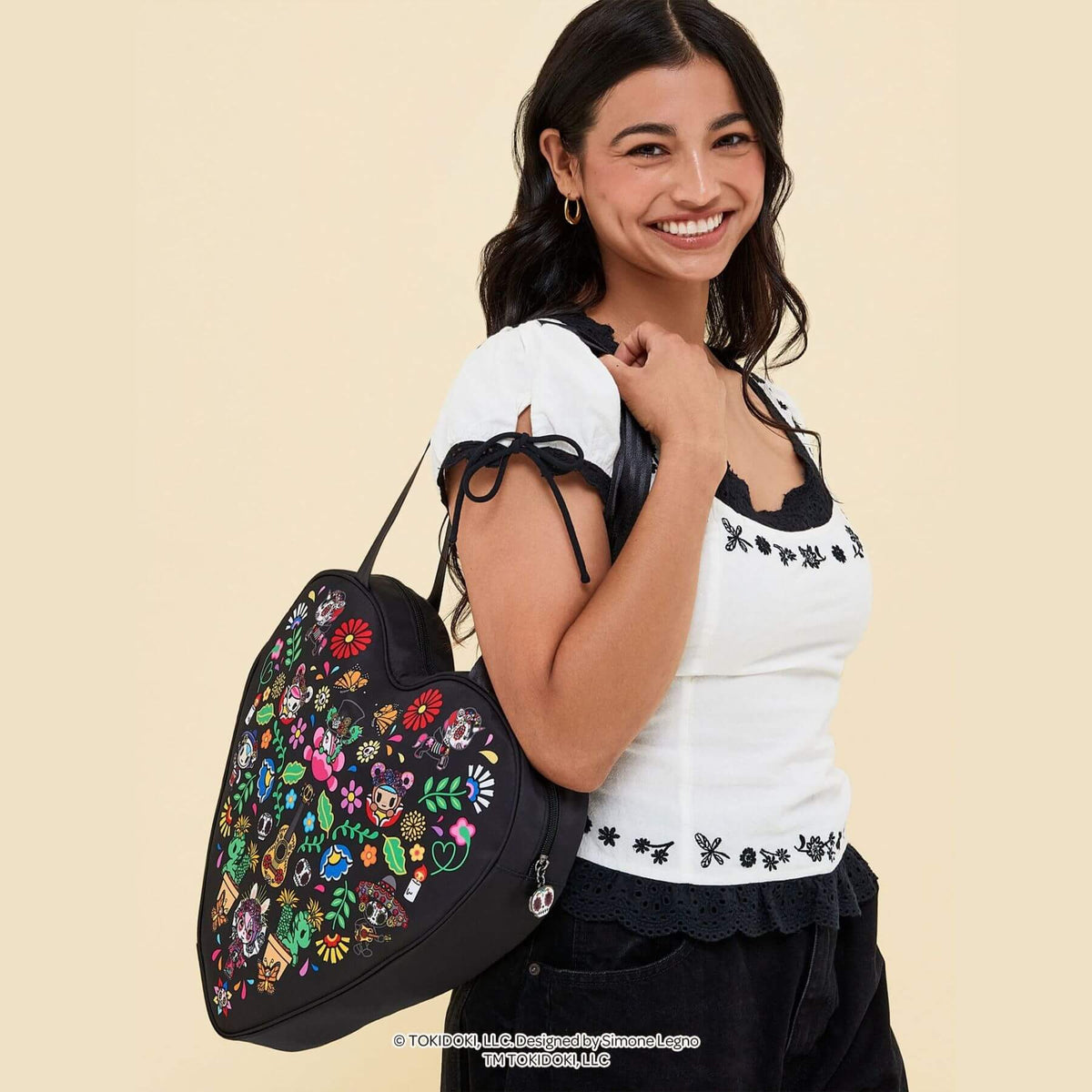 A smiling woman wearing a white embroidered top and black skirt carries tokidoki Heart Tote Diaper Bag – Dia de los Muertos