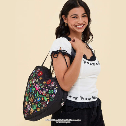 A smiling woman wearing a white embroidered top and black skirt carries tokidoki Heart Tote Diaper Bag – Dia de los Muertos