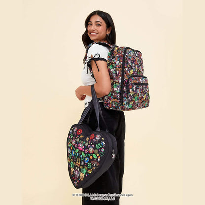 A woman wearing a white t-shirt and black pants is shown from the back, carrying a colorful floral backpack and tokidoki Heart Tote Diaper Bag – Dia de los Muertos