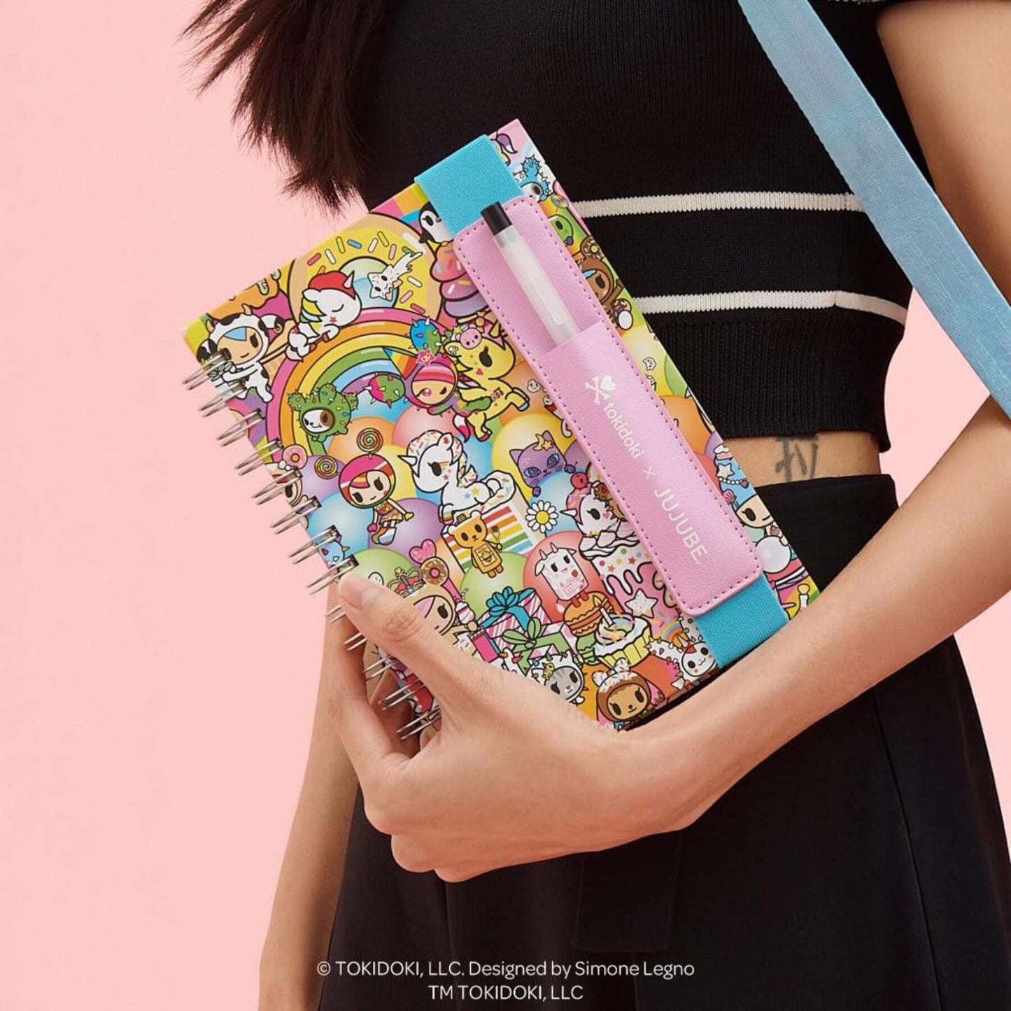 Colorful notebook with cartoon designs held by a person against a pink background