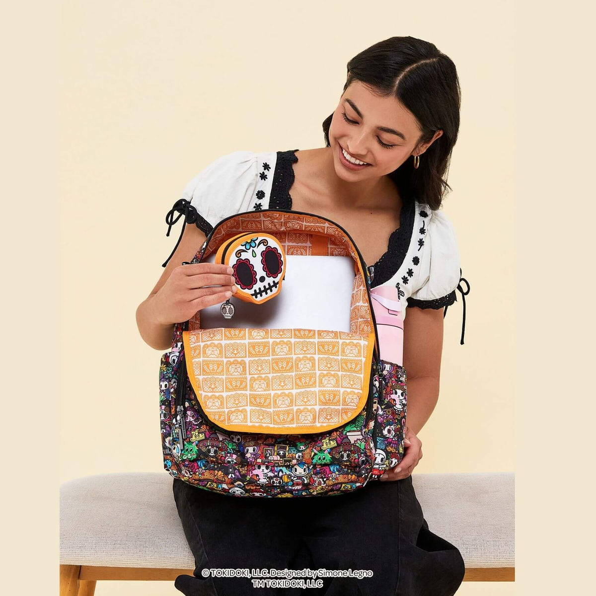 A woman wearing a white and black top holds a colorful Kuromi-patterned backpack with tokidoki Sugar Skull Mini Bag Clip-On Pouch Accessory – Dia de los Muertos