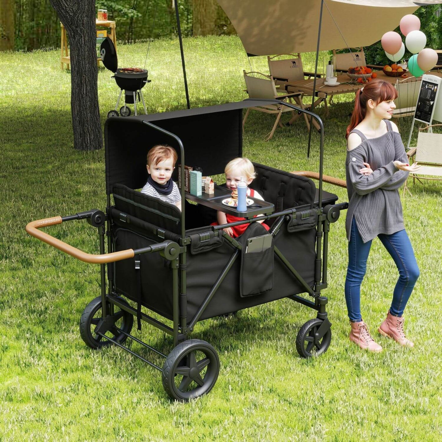 ToyRides Elite Wagon Stroller with 4-Seater - Black, shown on grass with two children seated inside and a woman standing beside it in a park setting.