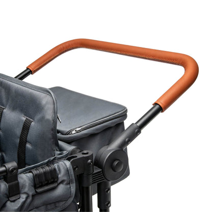 Close-up of a stroller handlebar with a curved brown faux-leather grip and black metal frame, attached to a dark gray stroller seat on a white background.
