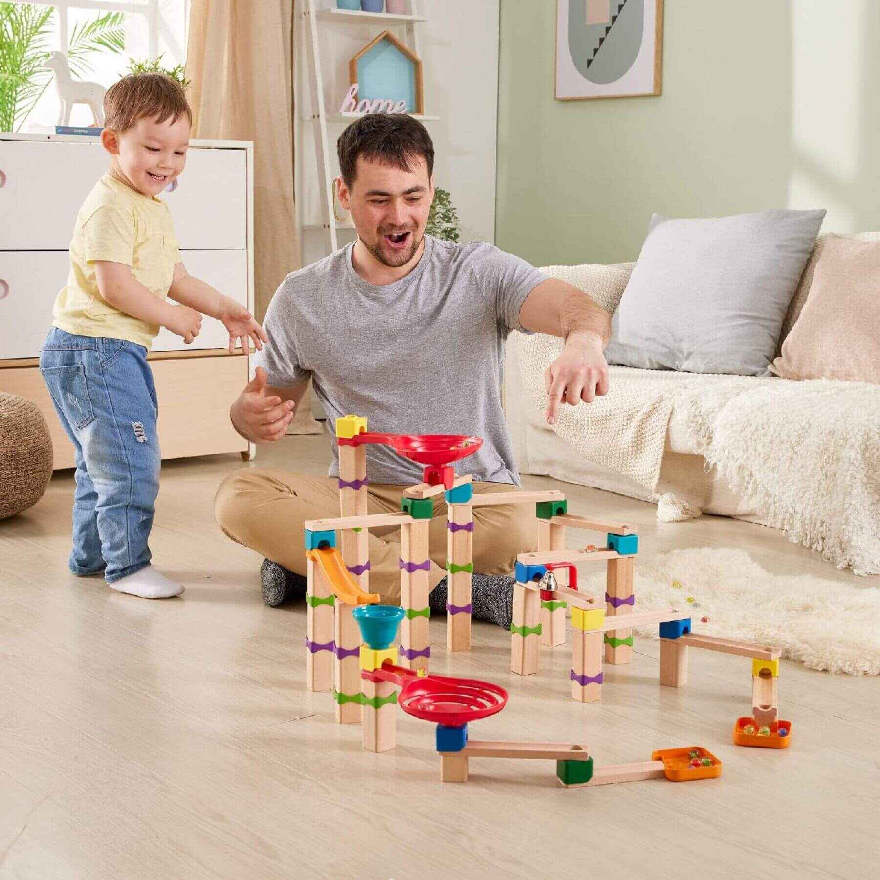 Man and child playing with Hape Tricks n Twists Marble Track in a living room.
