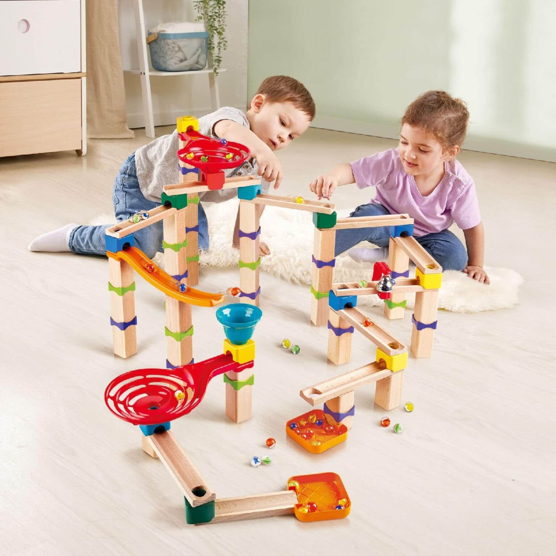 Two children playing with Hape Tricks n Twists Marble Track on a light-colored floor.