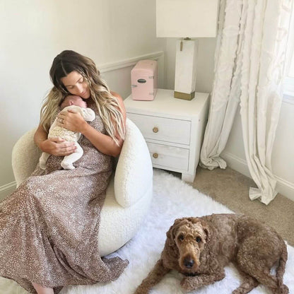 Woman in a sparkly dress holding a baby in a room with a dog on the floor.