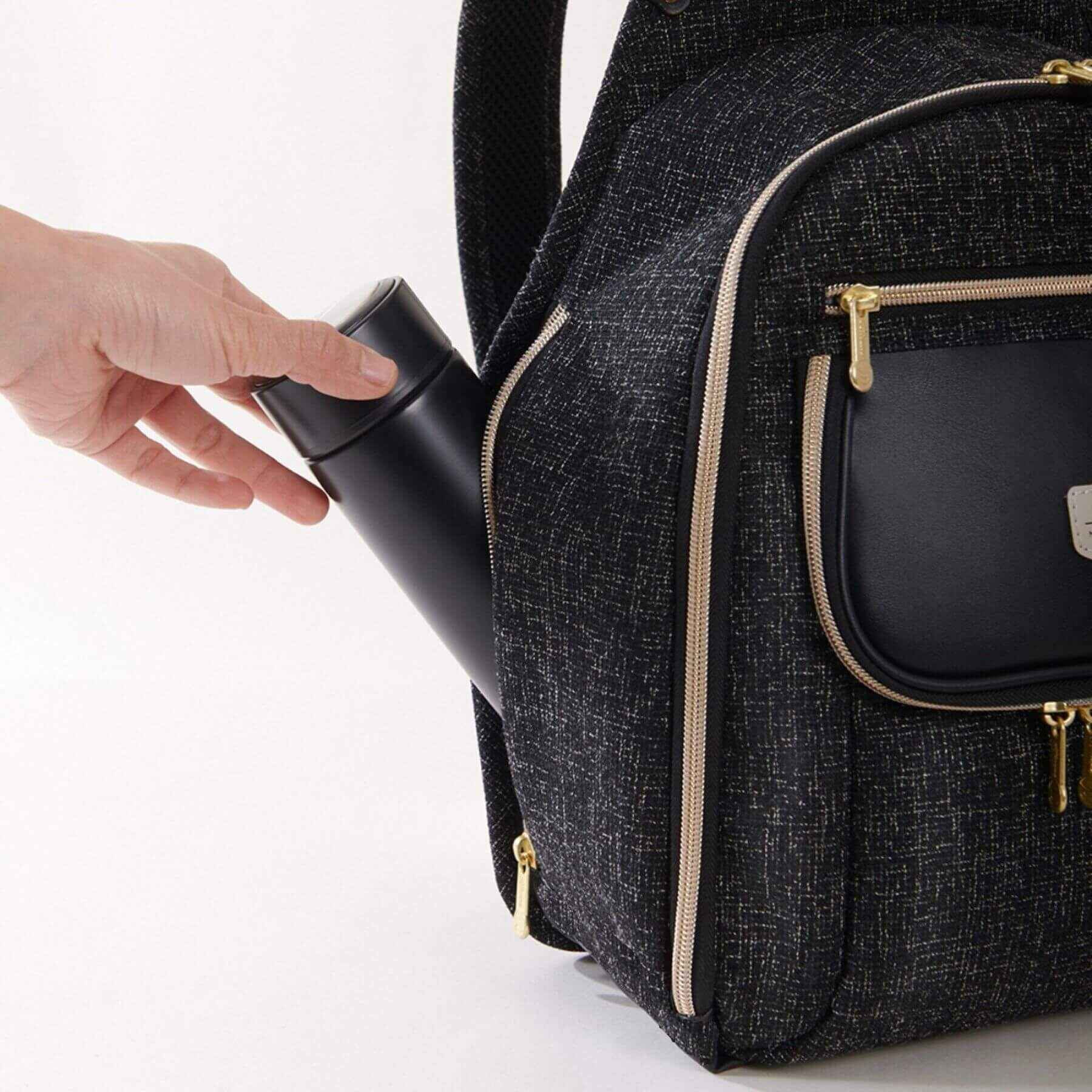 Sunveno Tweed Luxe Diaper Bag Backpack - Black with a hand placing a black container into one of its compartments on a white background