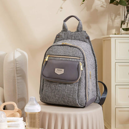 Sunveno Tweed Luxe Diaper Bag Backpack - Gray on a table with baby items in a room.