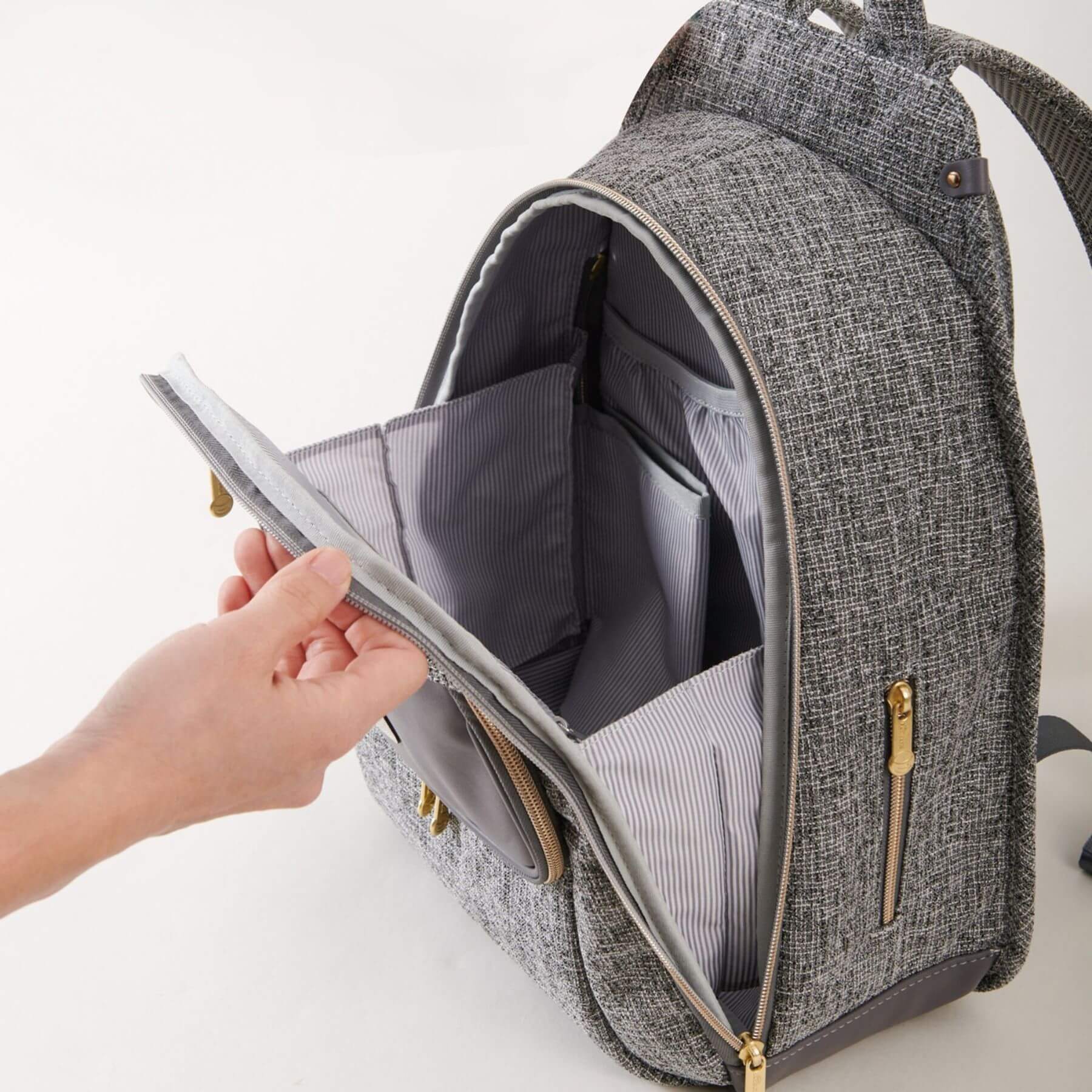 Sunveno Tweed Luxe Diaper Bag Backpack - Gray being opened by a hand on a white background
