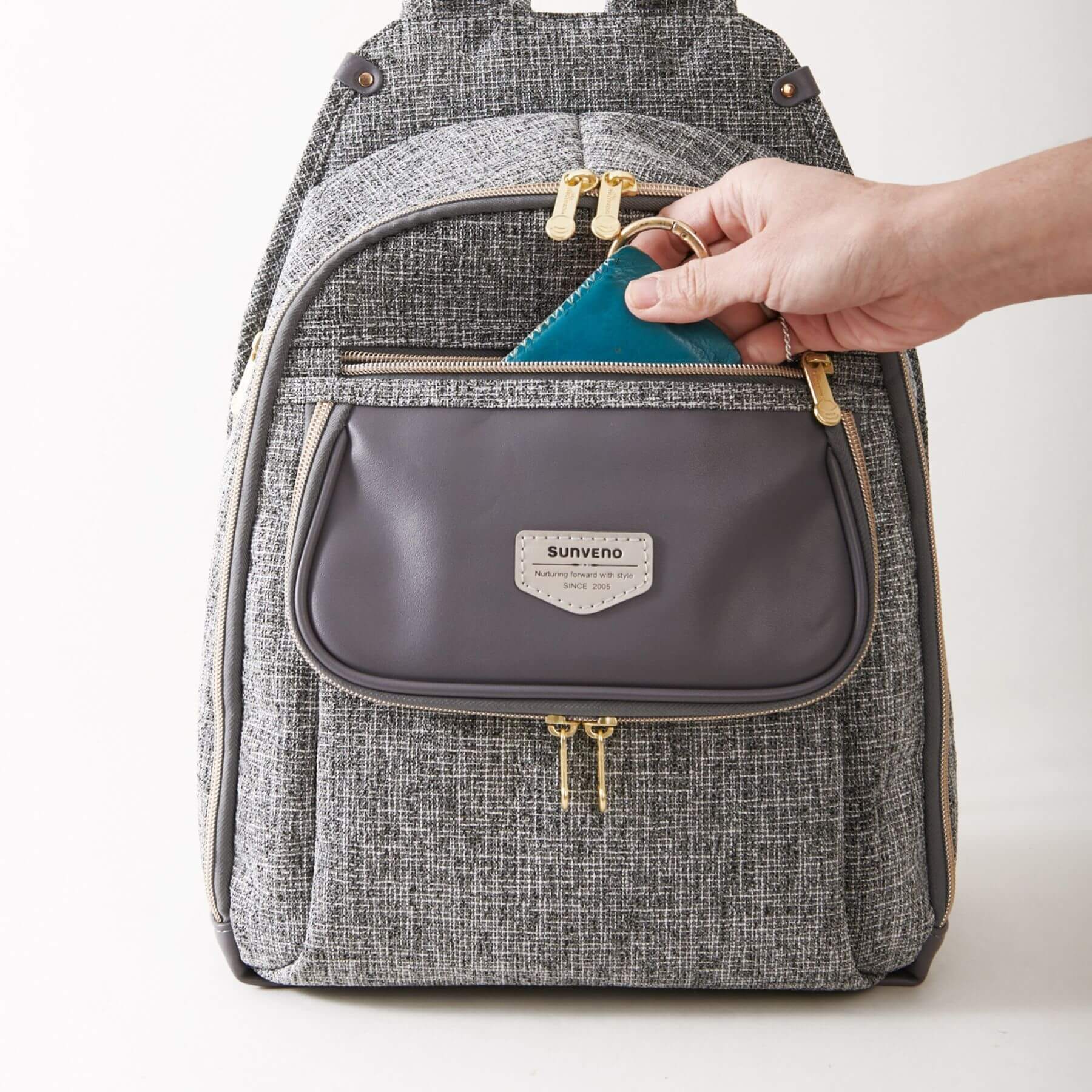 Sunveno Tweed Luxe Diaper Bag Backpack - Gray with a hand opening a small gray pouch, on a white background