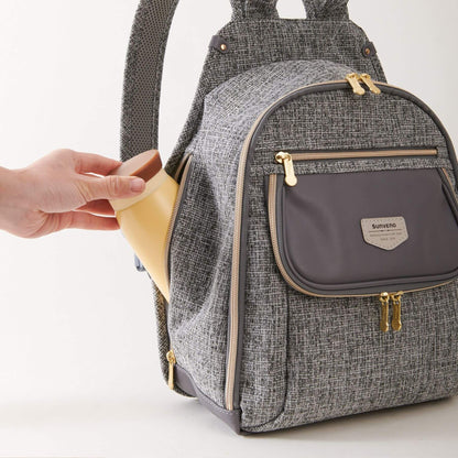 Sunveno Tweed Luxe Diaper Bag Backpack - Gray with a hand holding a yellow item, on a light gray background