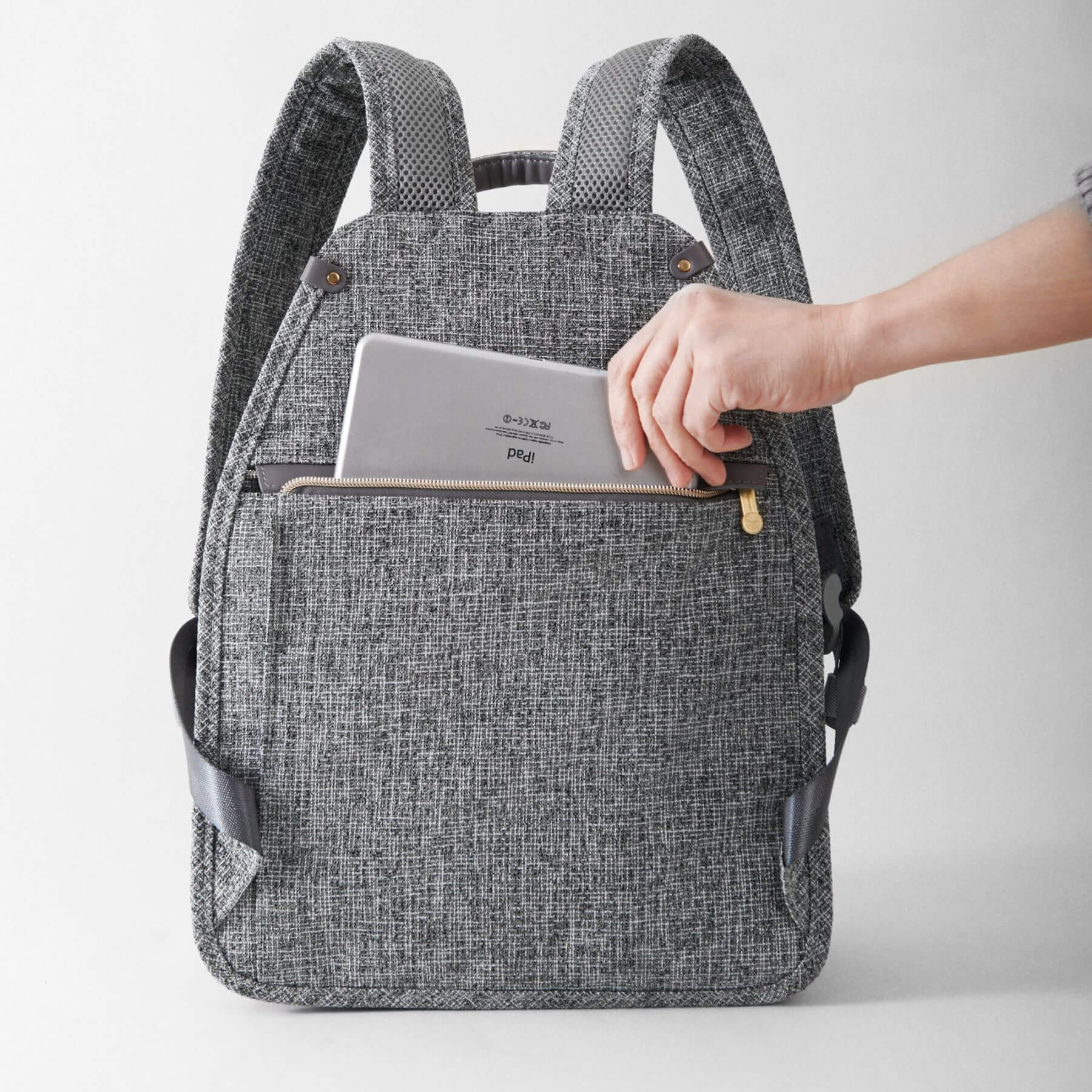 Sunveno Tweed Luxe Diaper Bag Backpack - Gray with a person placing a tablet into it on a light gray background
