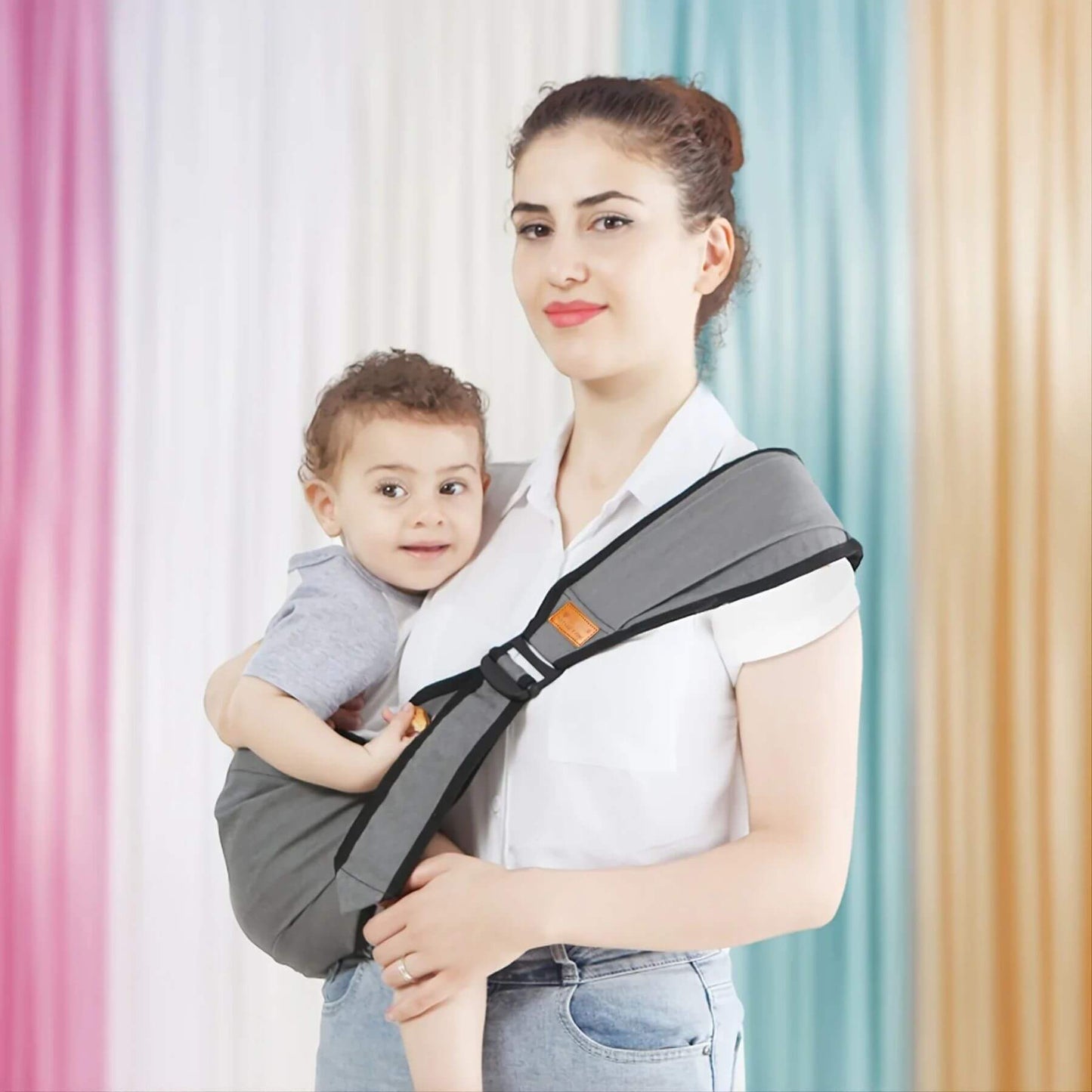 Woman holding a child using RocketBaby USA Universal Baby Carrier Grey against a colorful curtain background
