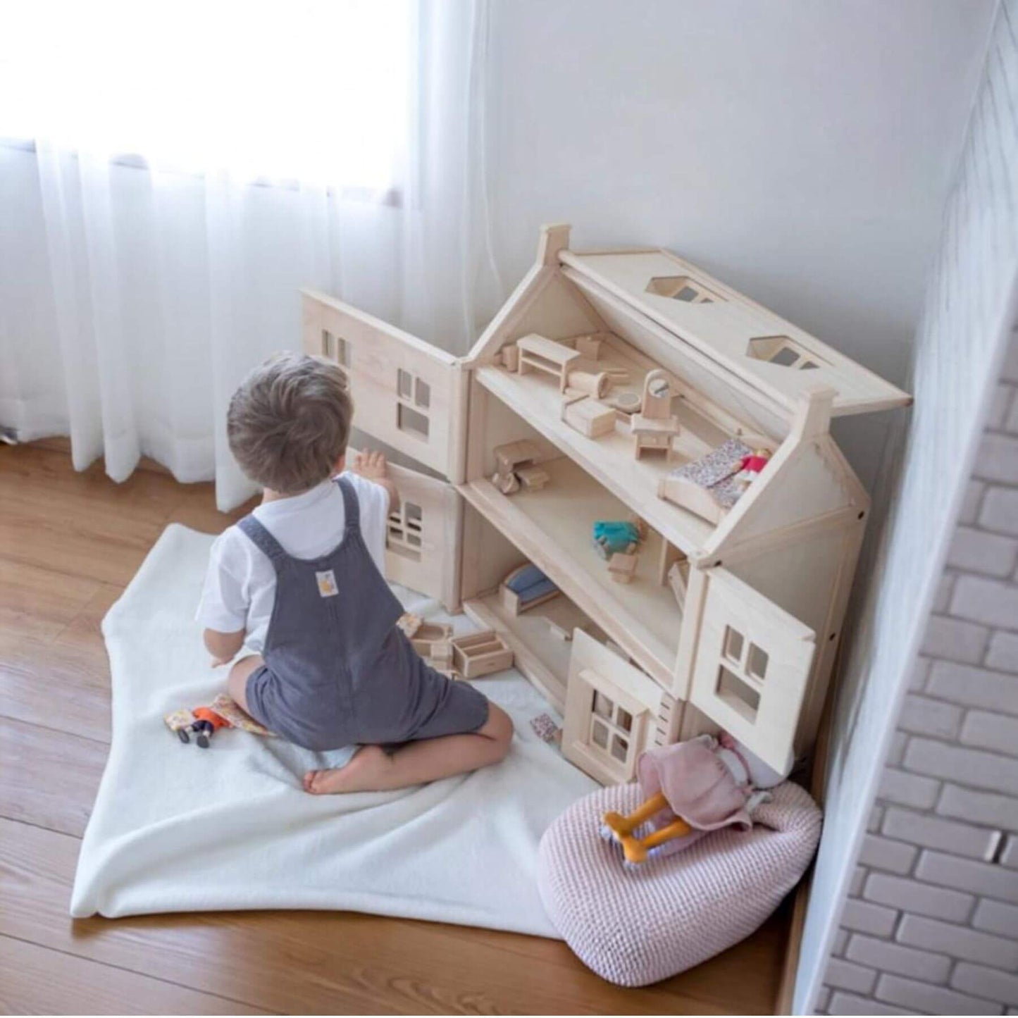 Child playing with PlanToys Victorian Dollhouse on a wooden floor.