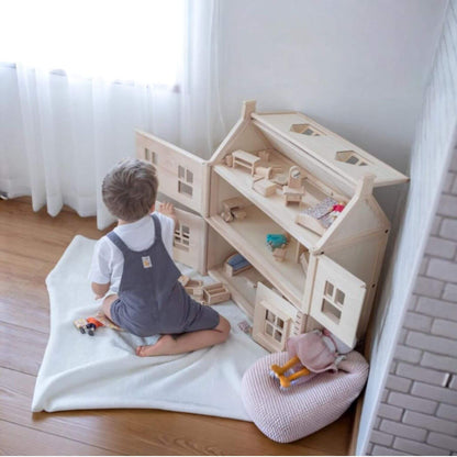 Child playing with PlanToys Victorian Dollhouse on a wooden floor.