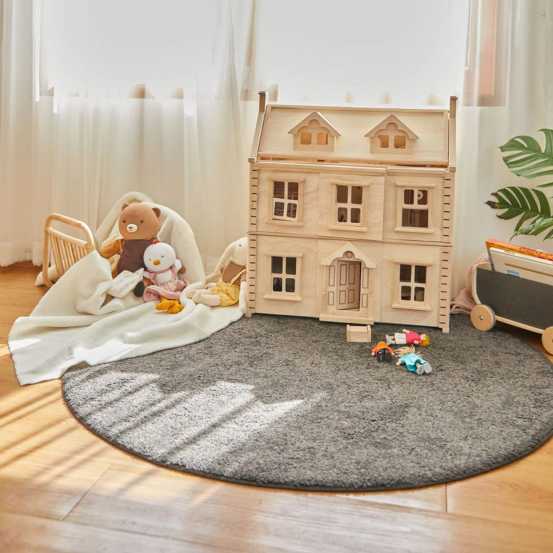 Children's playroom with PlanToys Victorian Dollhouse and toys on a gray round rug.