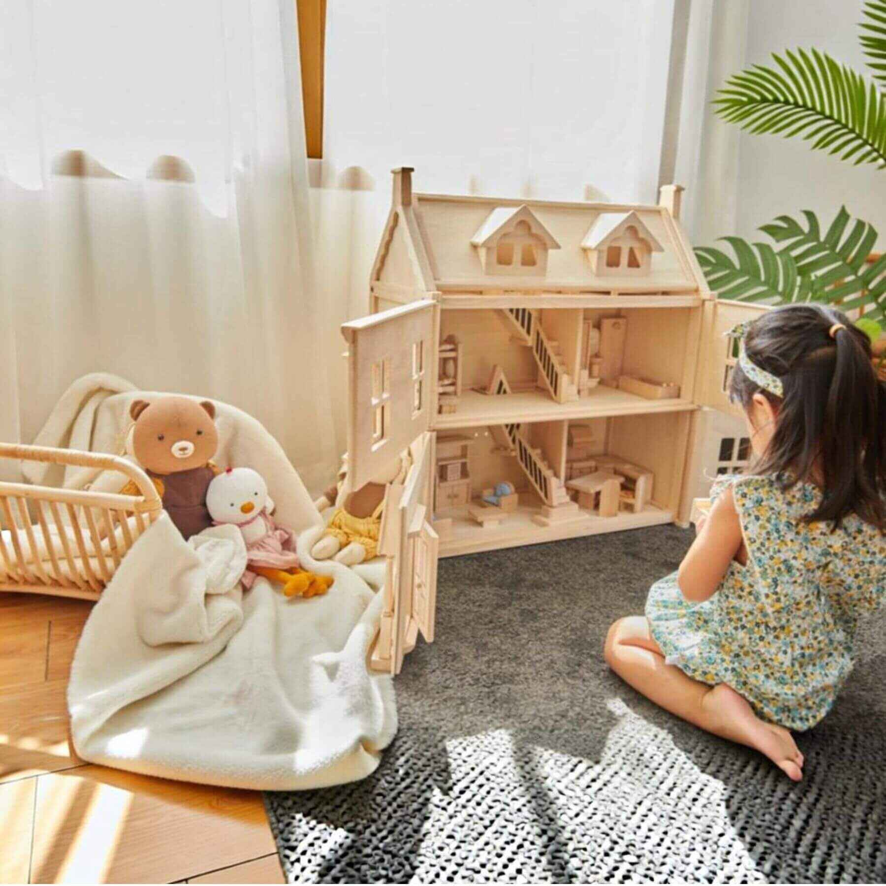 Child playing with PlanToys Victorian Dollhouse and stuffed animals in a cozy room.