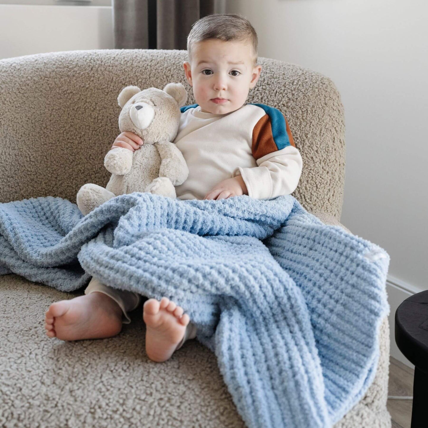 Child sitting on a couch with Saranoni Waffle Knit Toddler Blanket - Blue Jay and teddy bear