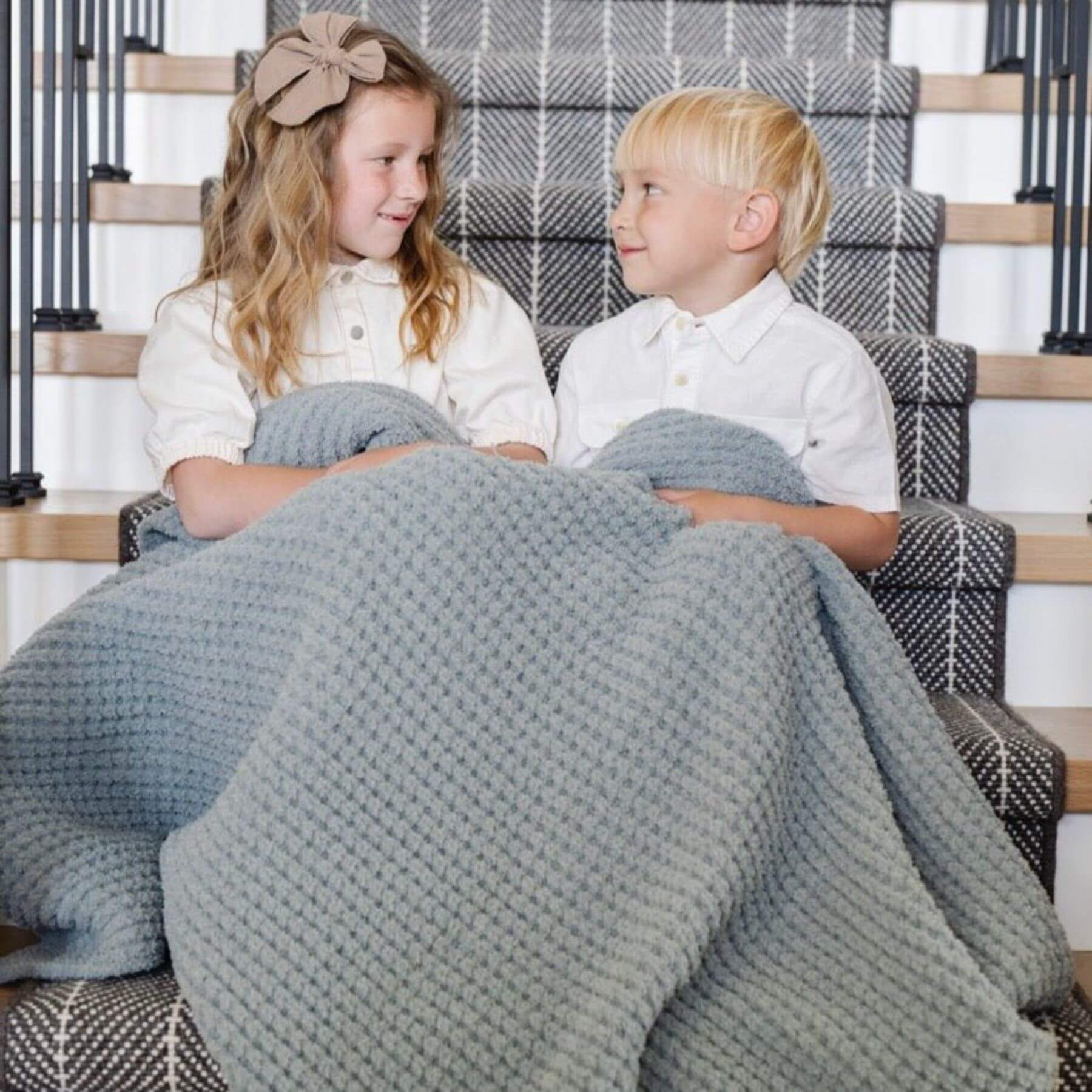 Two children sitting on a staircase with Saranoni Waffle Knit Toddler Blanket - Elm