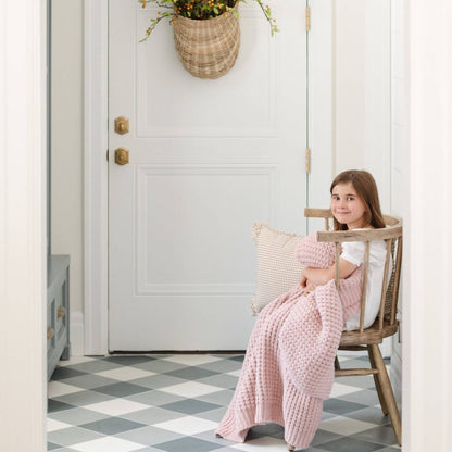 Young girl sitting in a chair holding Saranoni Waffle Knit Toddler Blanket - Rosette and pillow in a home setting.