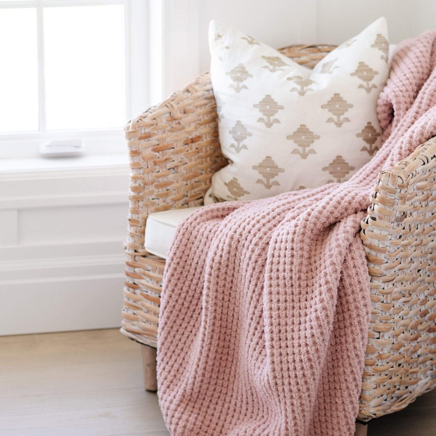 Wicker chair with pink blanket and patterned pillow in a bright room