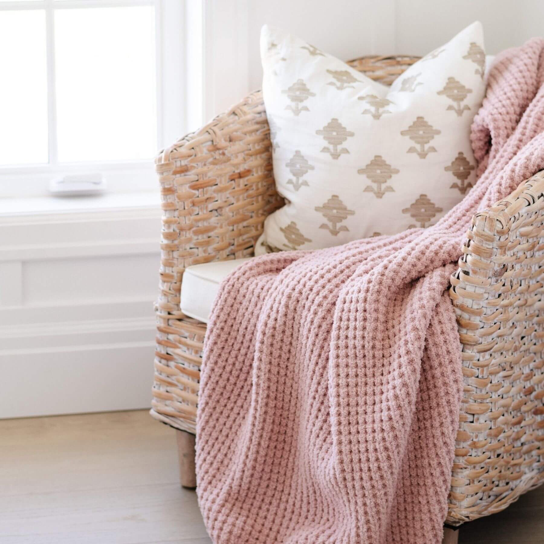 Wicker chair with pink blanket and patterned pillow in a bright room