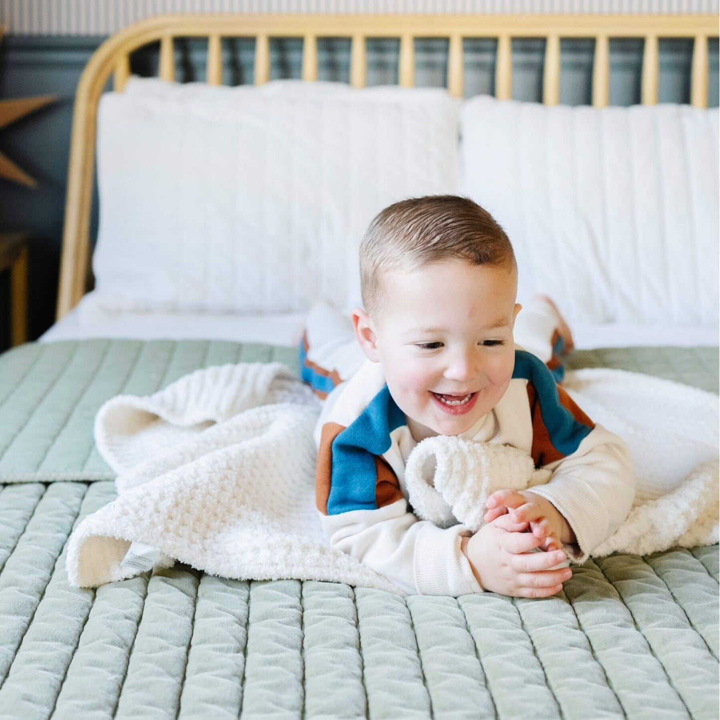 Child lying on a bed with Saranoni Waffle Knit Toddler Blanket - Swan and smiling