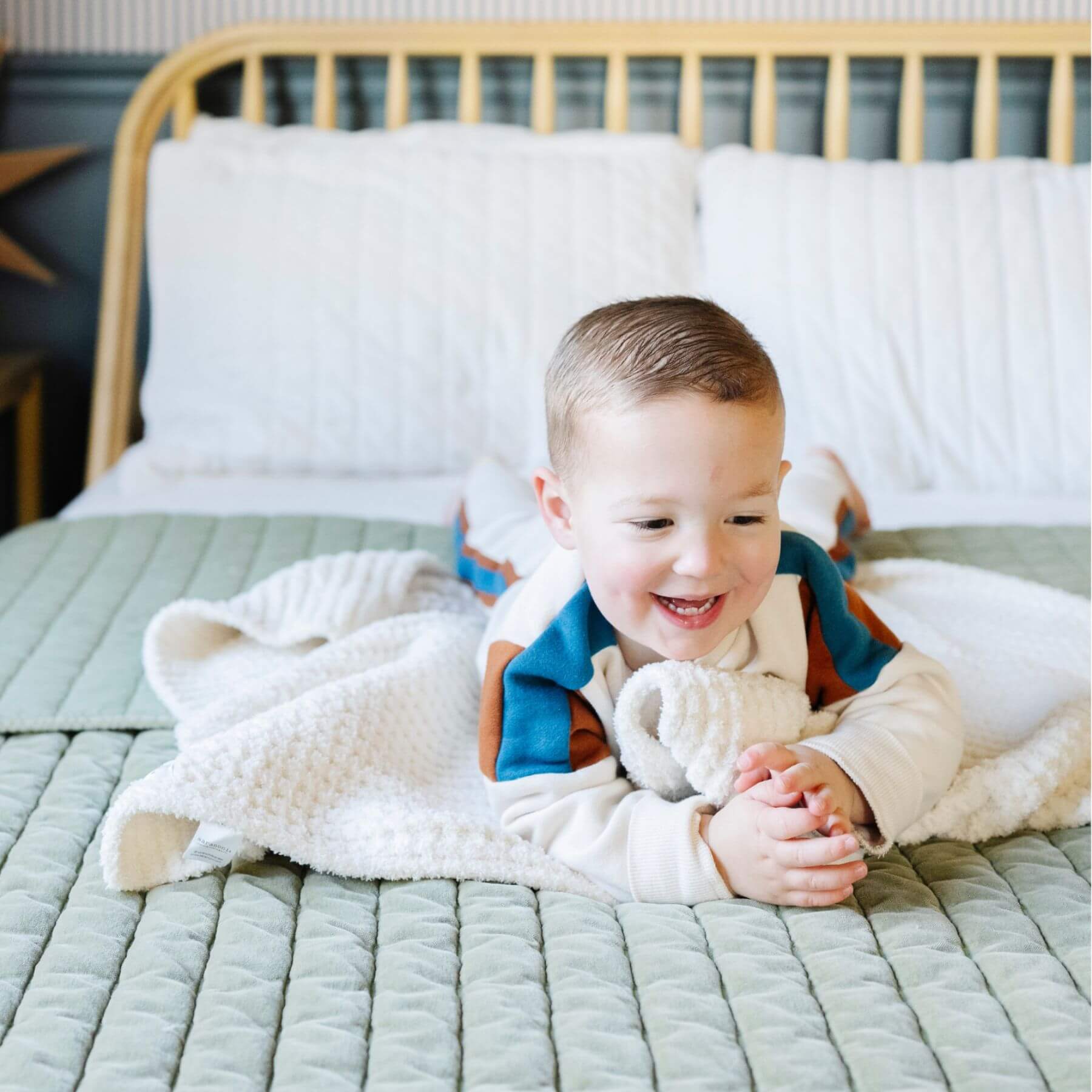 Child lying on a bed with Saranoni Waffle Knit Toddler Blanket - Swan and smiling