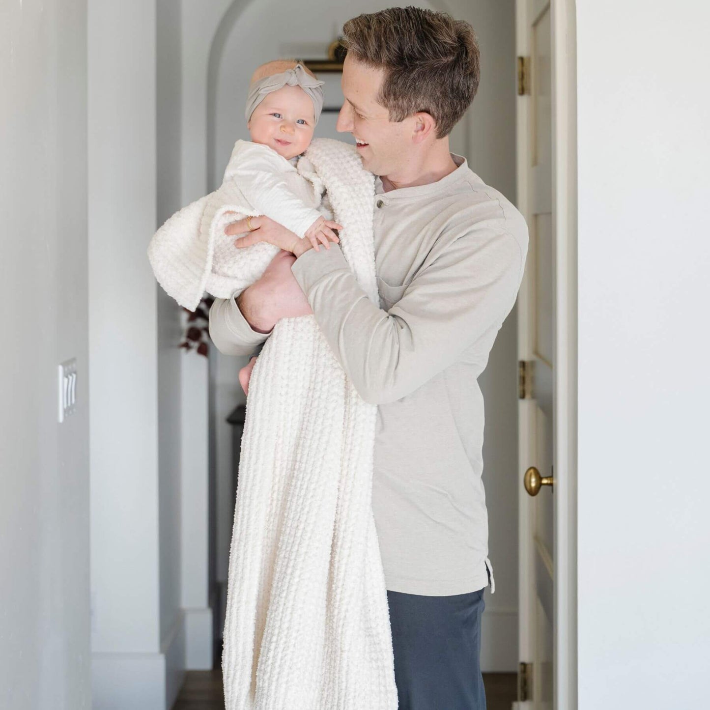 Man holding a baby wrapped in Saranoni Waffle Knit Toddler Blanket - Swan in a home setting