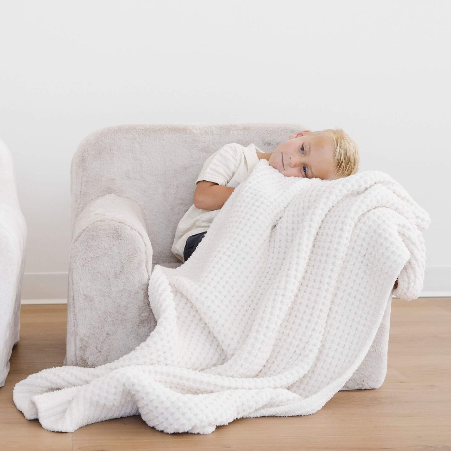 Person lying on a couch with Saranoni Waffle Knit Toddler Blanket - Swan draped over them in a minimalistic room.