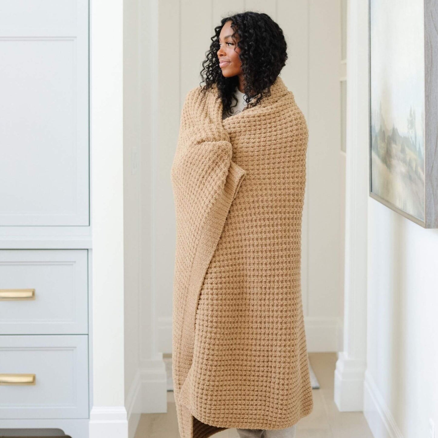 Woman wrapped in Saranoni Waffle Knit XL Throw Blanket - Allspice standing in a room with white walls and a window.