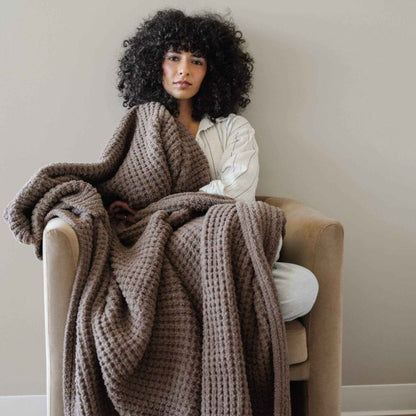 Woman sitting on a chair with Saranoni Waffle Knit XL Throw Blanket - Chestnut draped over her