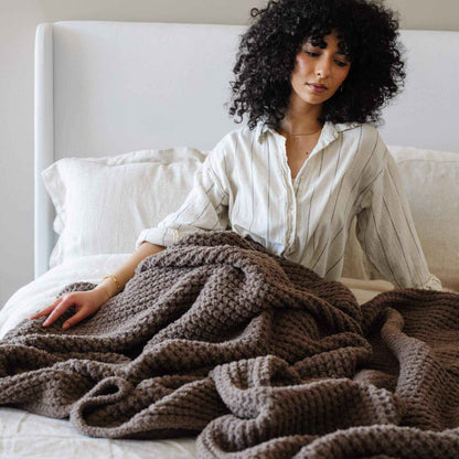 Woman sitting on a bed with Saranoni Waffle Knit XL Throw Blanket - Chestnut