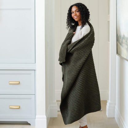 Woman wearing Saranoni Waffle Knit XL Throw Blanket - Thyme in a room with light gray walls and white trim.