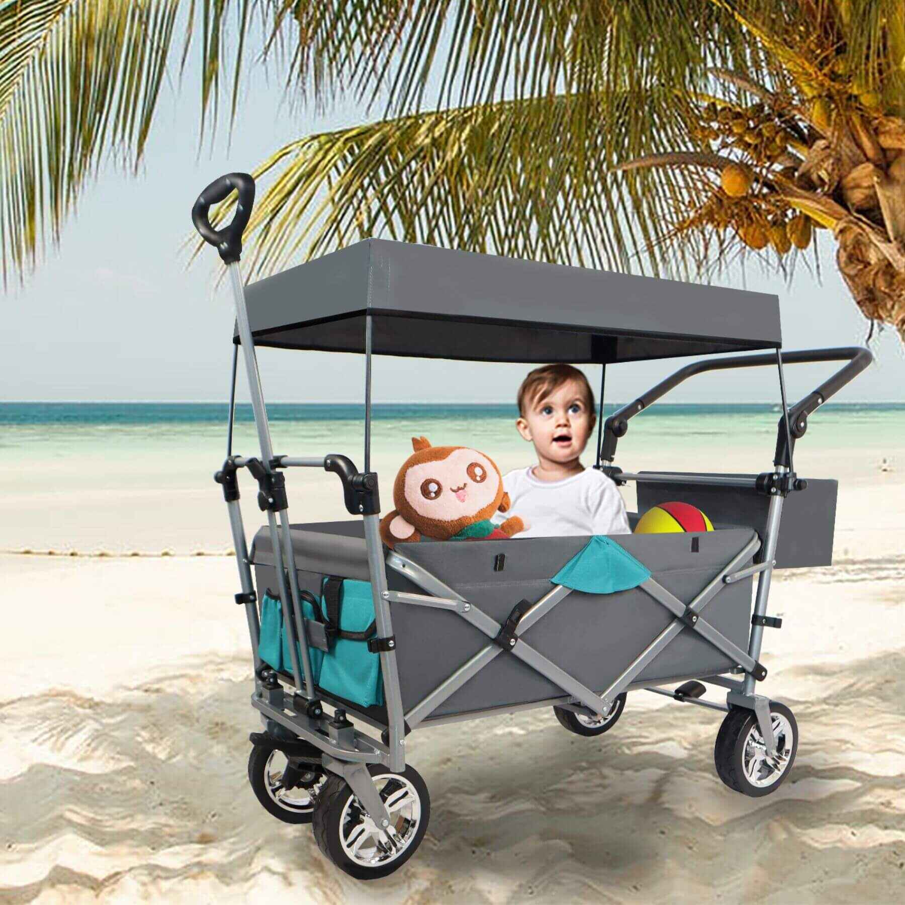 Child sitting in a gray folding wagon with canopy on a beach
