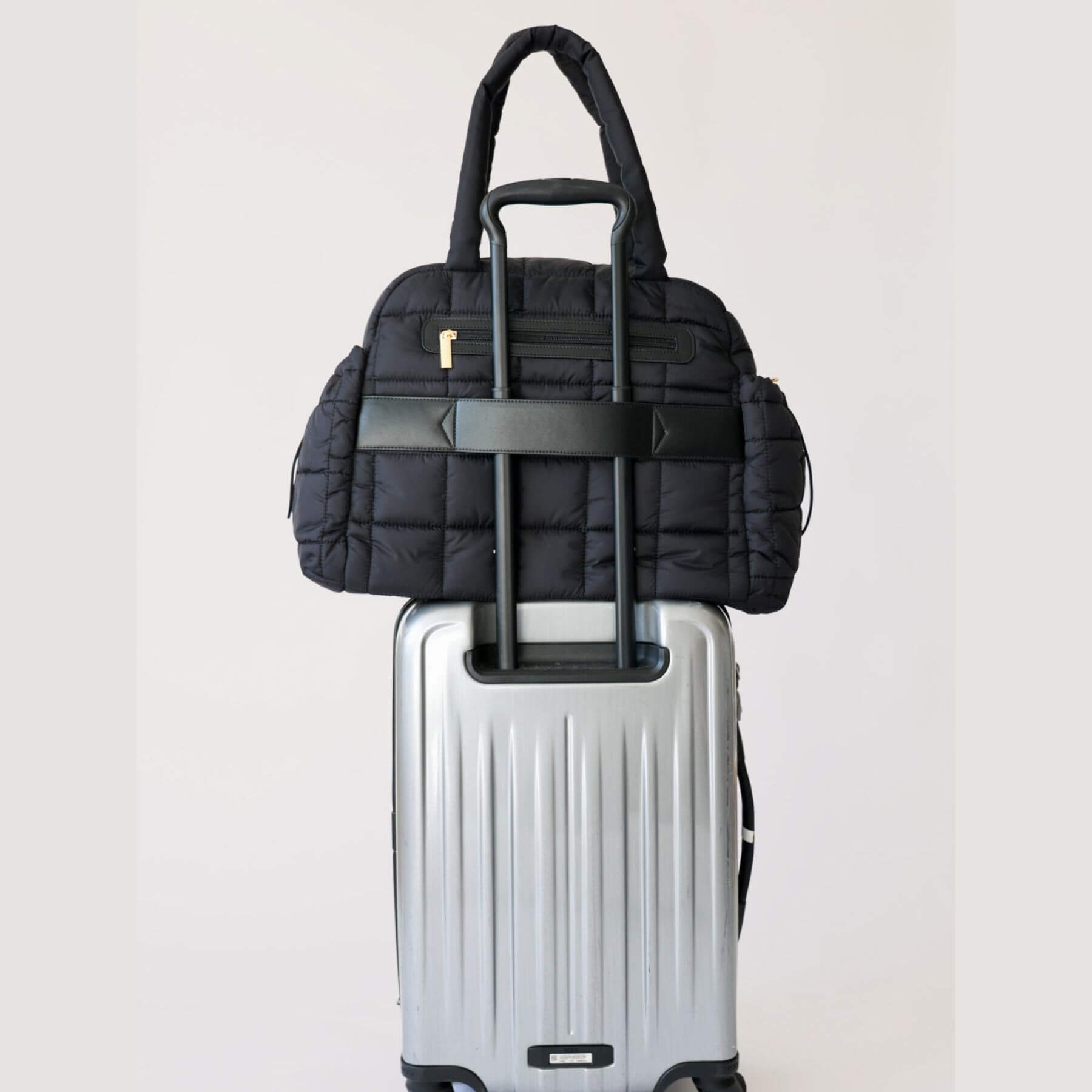 augustnoa the weekender duffle bag black on top of a silver suitcase against a white background