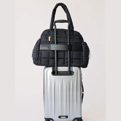 augustnoa the weekender duffle bag black on top of a silver suitcase against a white background
